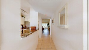 A hallway with a kitchen area on the left, a dining area in the middle, and a large mirror on the right. - Venice Condo, Pool, Balcony & Beaches Nearby! (Venice)