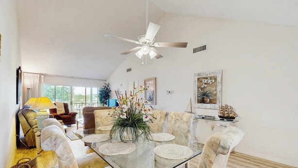 A spacious living room with a glass-top coffee table, comfortable seating, a ceiling fan, and a large window providing natural light. - Venice Condo, Pool, Balcony & Beaches Nearby! (Venice)