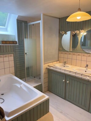 Une salle de bain avec une baignoire, deux lavabos, une douche et un grand miroir.