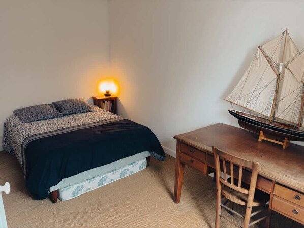 Una camera da letto con un letto, un comodino, una lampada e un modellino di nave.