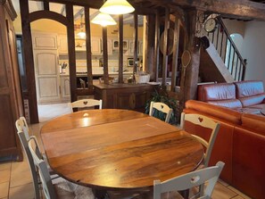 Une table de salle à manger en bois avec des chaises, un canapé en cuir et un escalier orné d’une horloge.