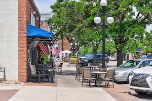 A sidewalk cafe with outdoor seating, American flags, and parked cars.