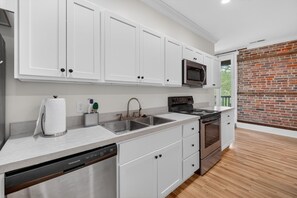 A modern kitchen with white cabinets, stainless steel appliances, and a brick wall. - River Room Getaway On Front Street - Suite C 1 Bedroom Apts (Georgetown)