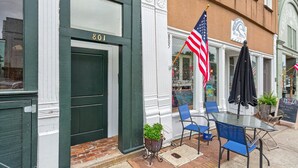 Ein Gebäude mit einer grünen Tür, auf der '801' steht, einer amerikanischen Flagge und einem Tisch mit blauen Stühlen davor.