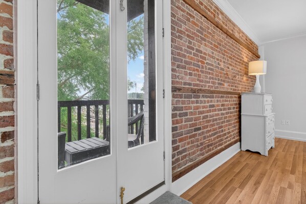 A room with a brick wall, a white door with glass panels, a small white dresser, and a wooden floor.