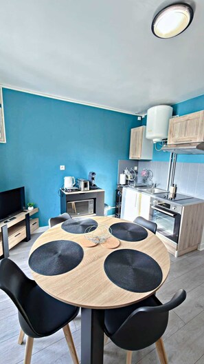 Une cuisine compacte dotée d’appareils électroménagers modernes, un coin repas avec une table ronde et des chaises noires, et un mur d’accent bleu.