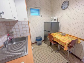Ett litet pentry med en diskho, ett kylskåp, ett fönster och ett bord med en duk på.