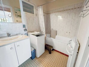 Ett litet badrum med handfat, tvättmaskin och badkar.
