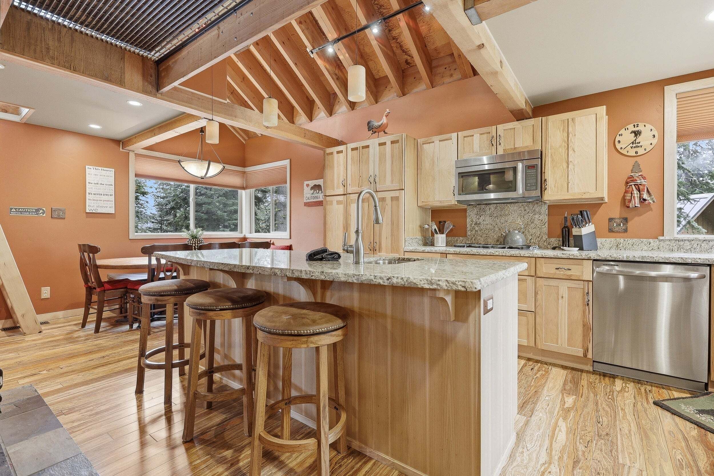 A kitchen with wooden cabinets, a stainless steel dishwasher, a microwave, and a bar area with stools.