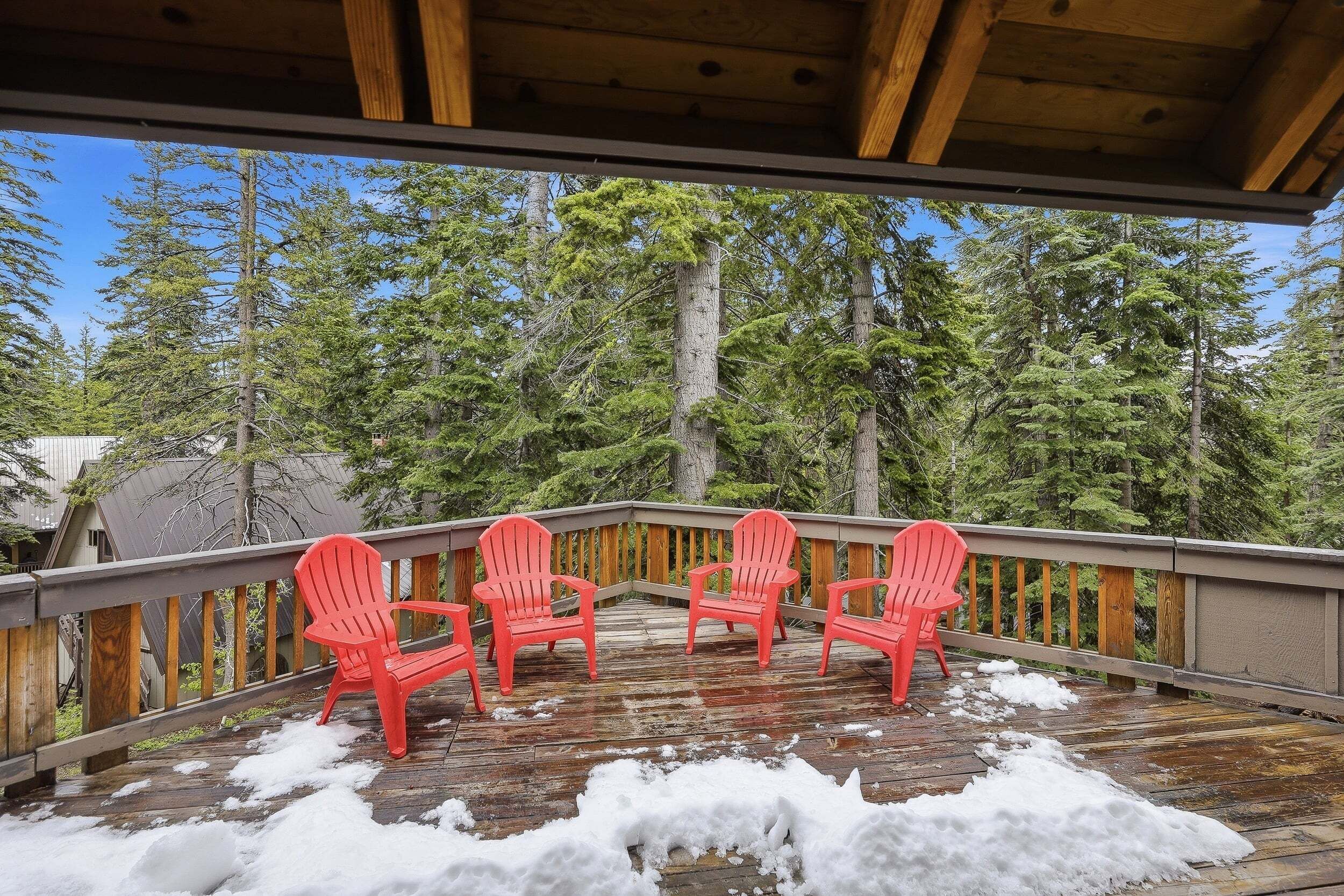 A wooden deck with four red chairs, surrounded by a forest.
