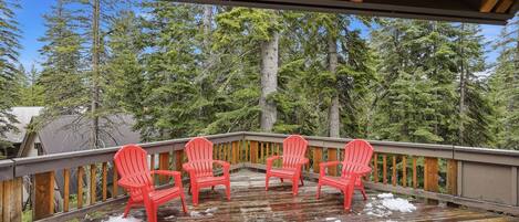 A wooden deck with four red chairs, surrounded by a forest.