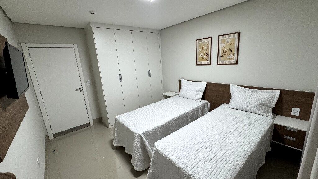 Een slaapkamer met twee enkele bedden, een garderobe en twee ingelijste foto’s aan de muur.