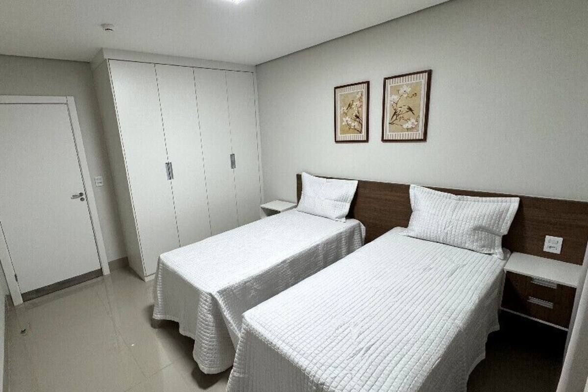 Une chambre avec deux lits simples, une armoire et deux tableaux encadrés au mur.