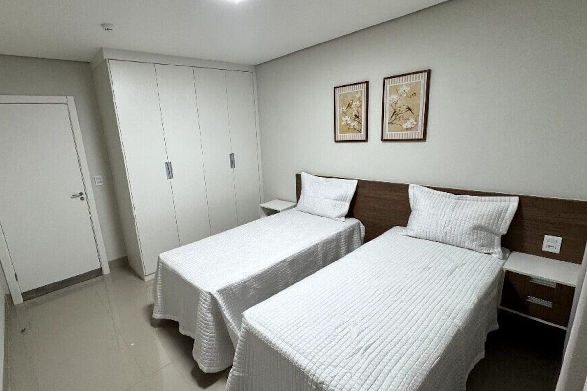 Une chambre avec deux lits simples, une armoire et deux tableaux encadrés au mur.