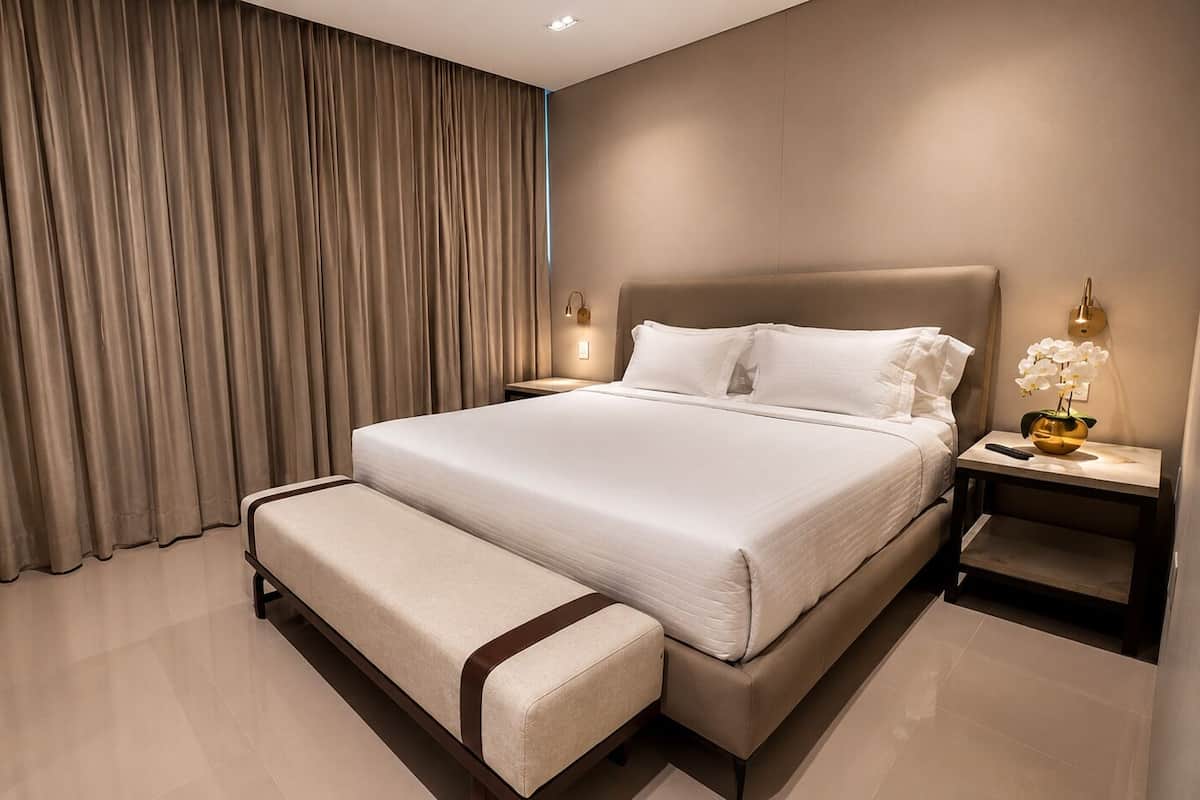 Une chambre d’hôtel moderne avec un grand lit, une table de chevet avec une lampe et une fenêtre avec des rideaux.