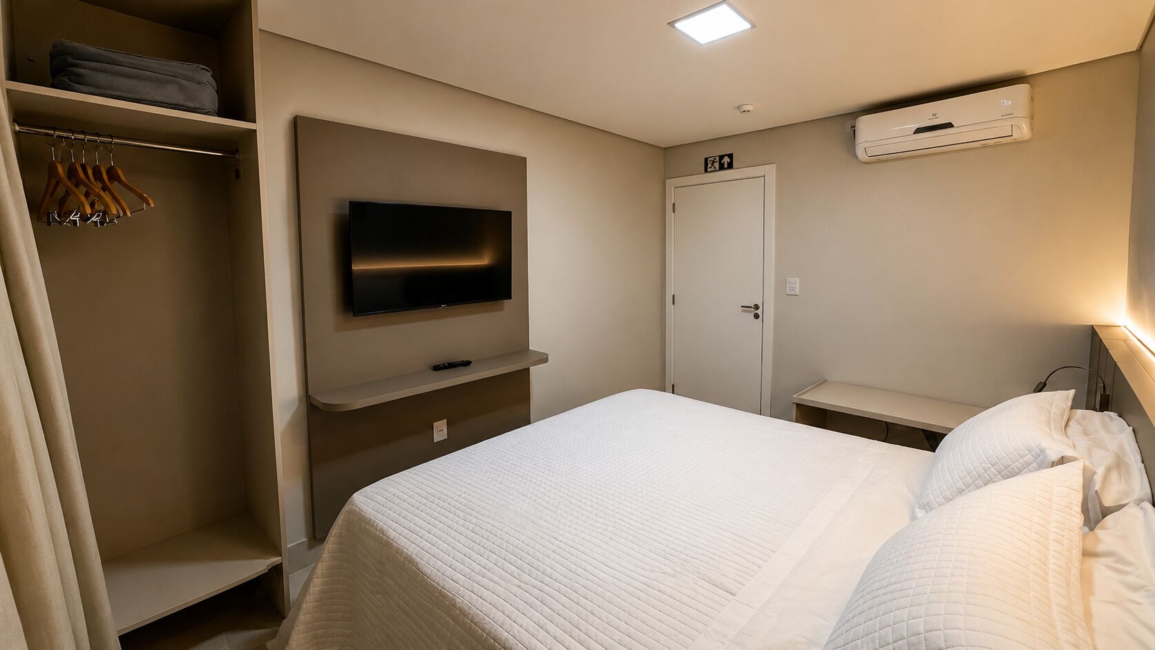 Ett hotellrum med en säng, en tv som är monterad på väggen, en garderob och en luftkonditioneringsanläggning.