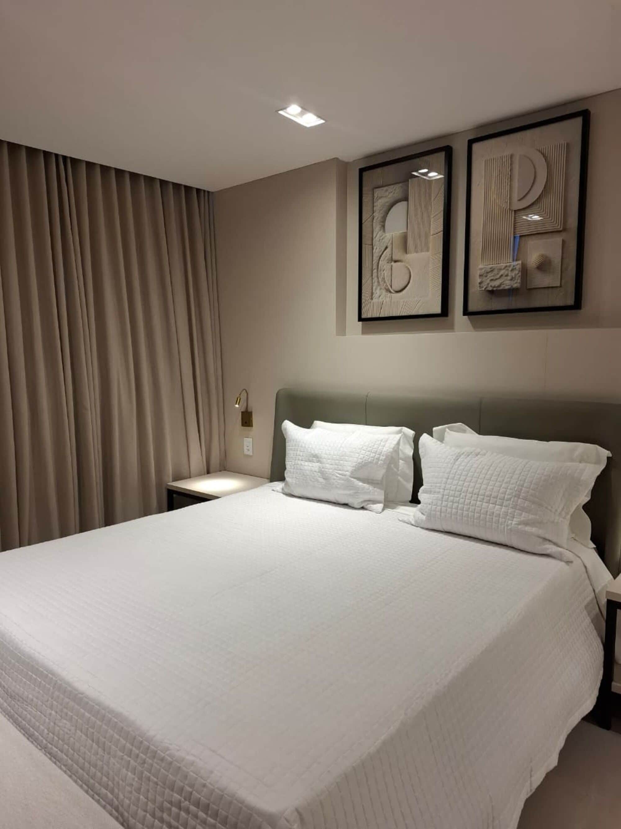 A hotel room with a large bed, a nightstand, a lamp, and two framed artworks on the wall.
