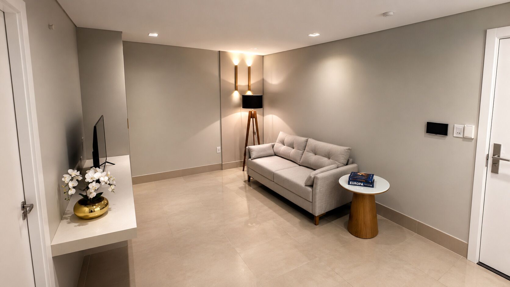A modern living room with a sofa, a small round table, a lamp, and a vase with flowers.