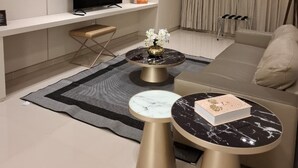 Un salon moderne doté d’un téléviseur à écran plat, d’un canapé, de deux tables basses et d’une grande fenêtre agrémentée de rideaux.