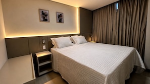 Una habitación de hotel moderna con una cama grande, mesitas de noche, una lámpara de pared y dos cuadros enmarcados.