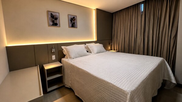 A modern hotel room with a large bed, bedside tables, a wall-mounted light, and two framed pictures.