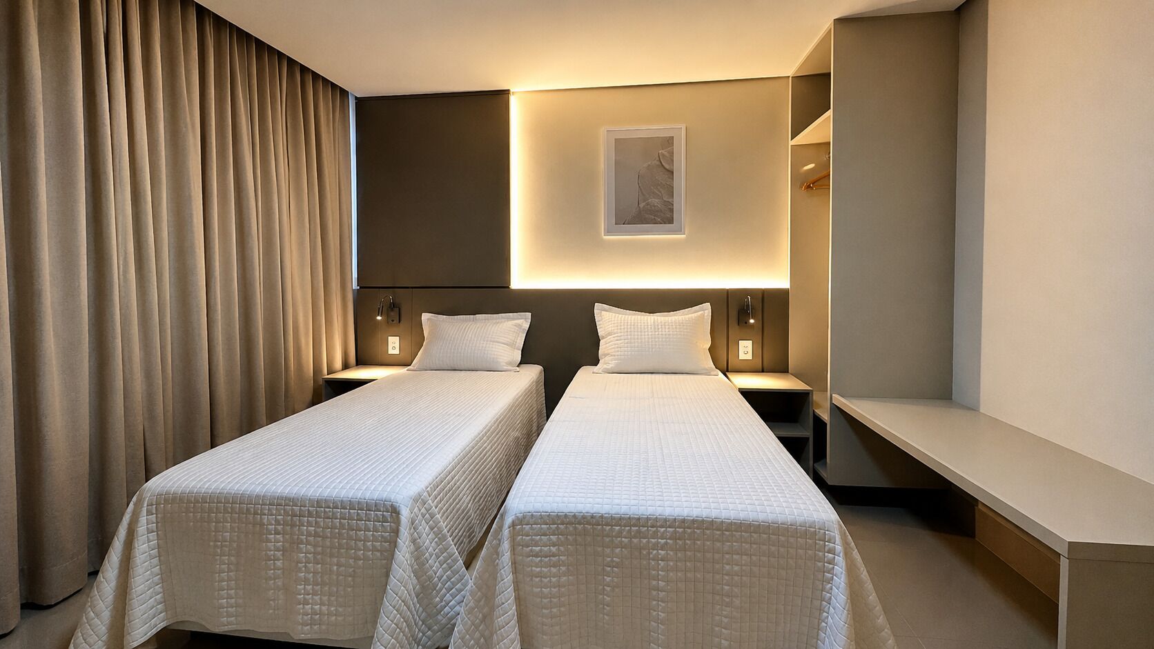 Une chambre d’hôtel avec deux lits, une table de chevet, une petite table, une lampe fixée au mur et un tableau encadré.