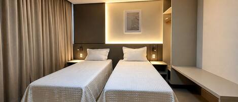 Une chambre d’hôtel avec deux lits, une table de chevet, une petite table, une lampe fixée au mur et un tableau encadré.