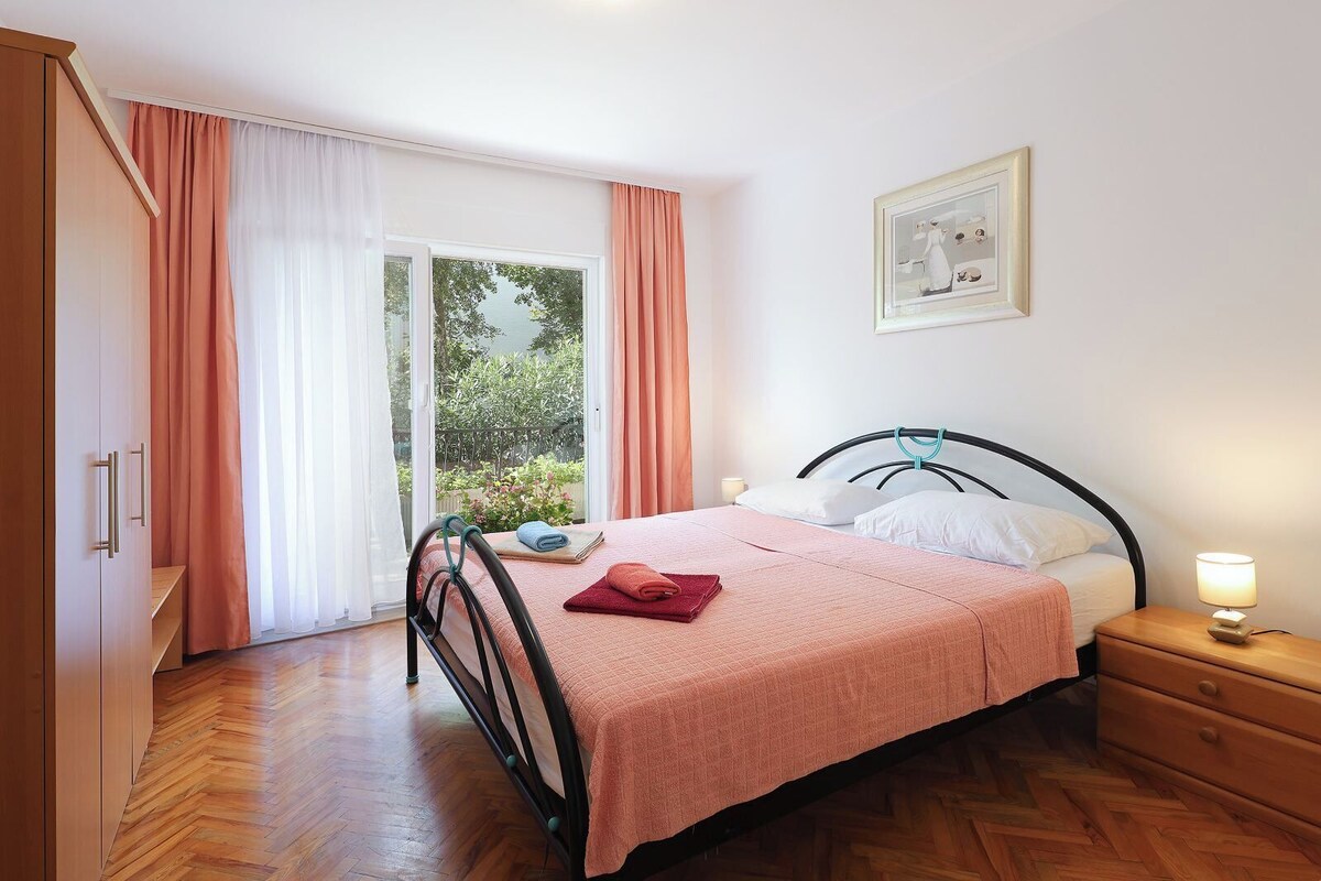 Ein Schlafzimmer mit Bett, Nachttisch, Lampe, Kleiderschrank und einer Schiebetür, die auf einen Balkon führt.