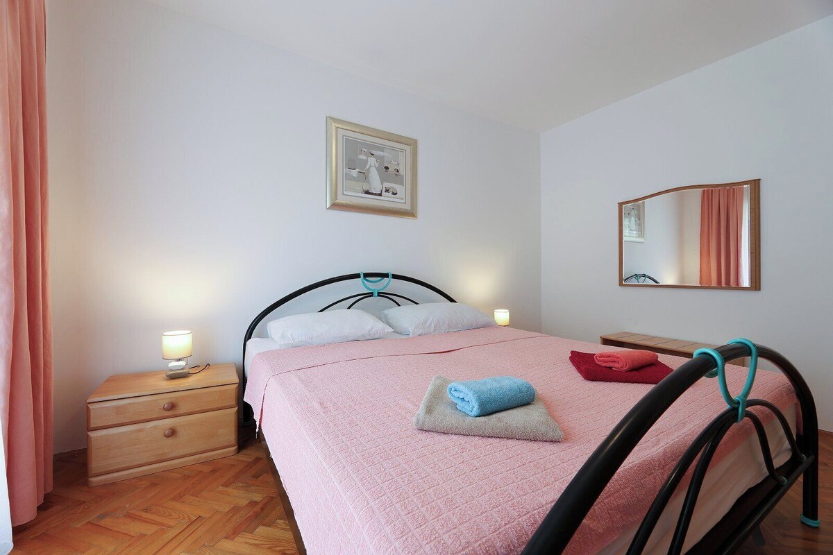 Ein Schlafzimmer mit einem Bett, Nachttischen, einem Schminktisch, einem Spiegel und einem gerahmten Bild an der Wand.