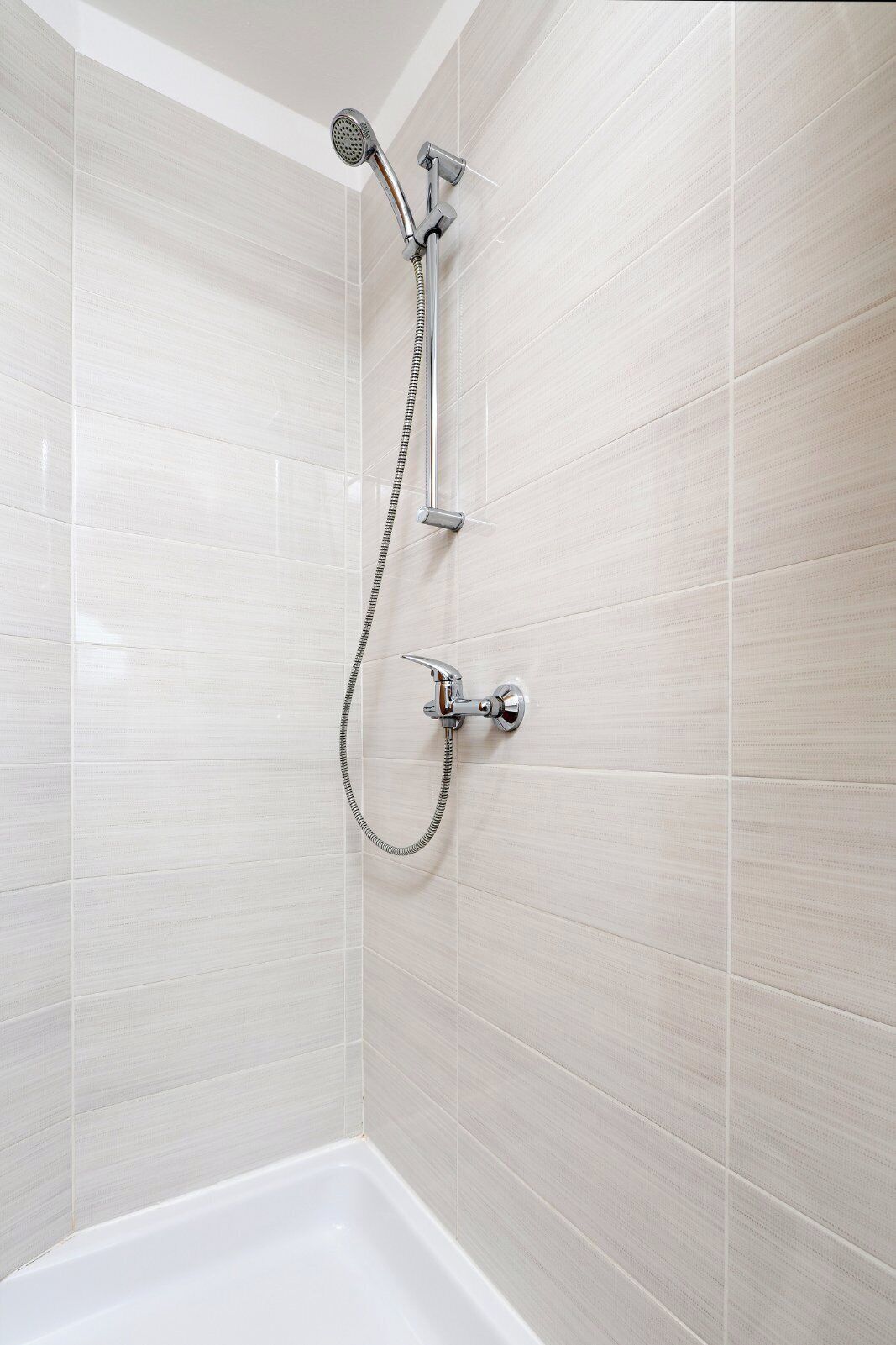 A shower with a handheld showerhead and a wall-mounted faucet.