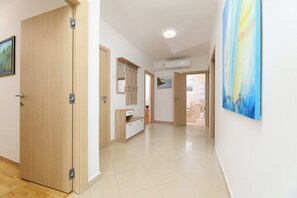 A hallway with wooden doors, a white wall, and a painting. - Apartmani Pintar (Jadranovo)