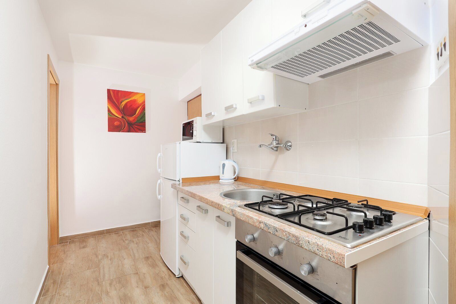 Une cuisine compacte avec des meubles blancs, une cuisinière à gaz, un four à micro-ondes et une bouilloire.