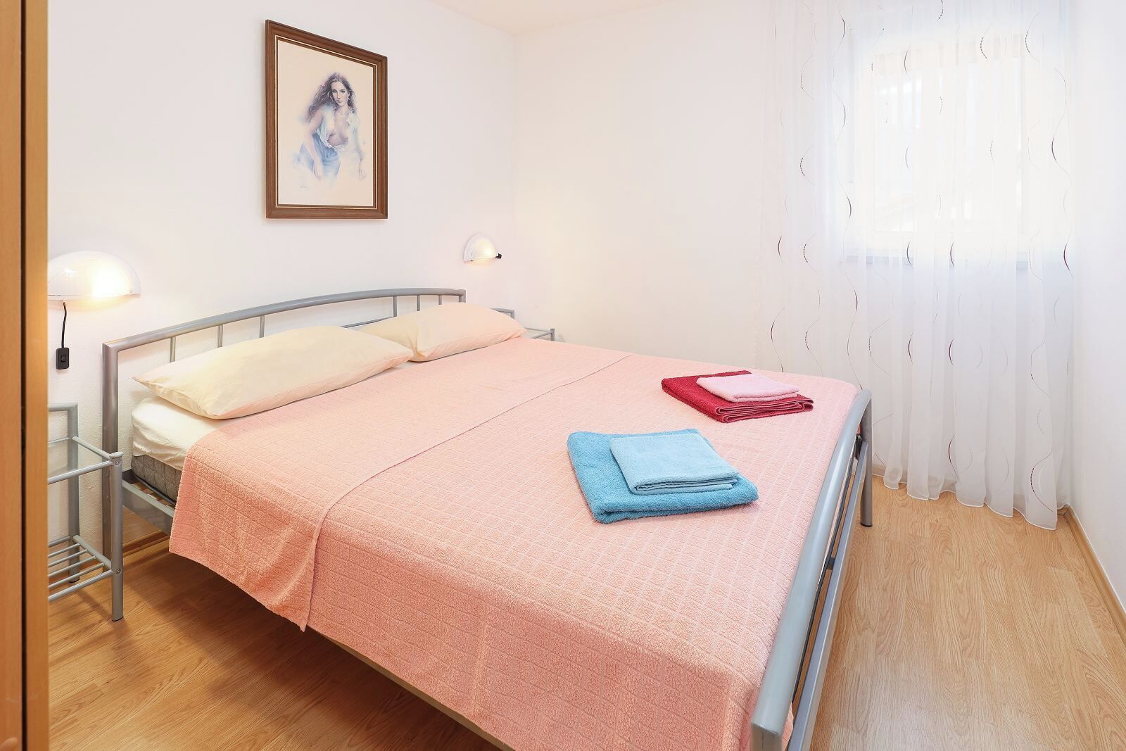 Ein Einzelbett mit rosa Bettdecke, zwei Kissen und zwei gefaltete Handtücher.