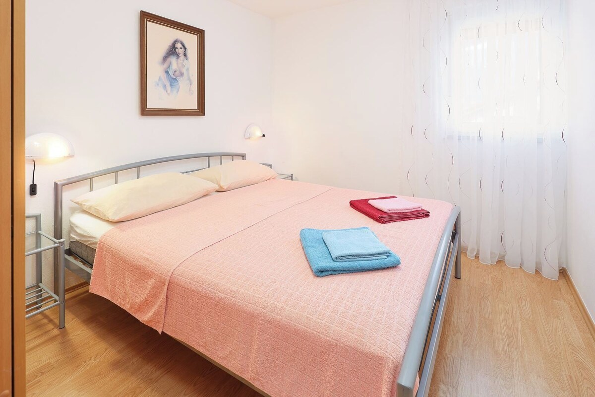 Ein Einzelbett mit rosa Bettdecke, zwei Kissen und zwei gefaltete Handtücher.
