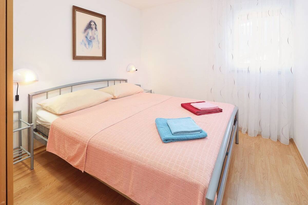 Ein Einzelbett mit rosa Bettdecke, zwei Kissen und zwei gefaltete Handtücher.