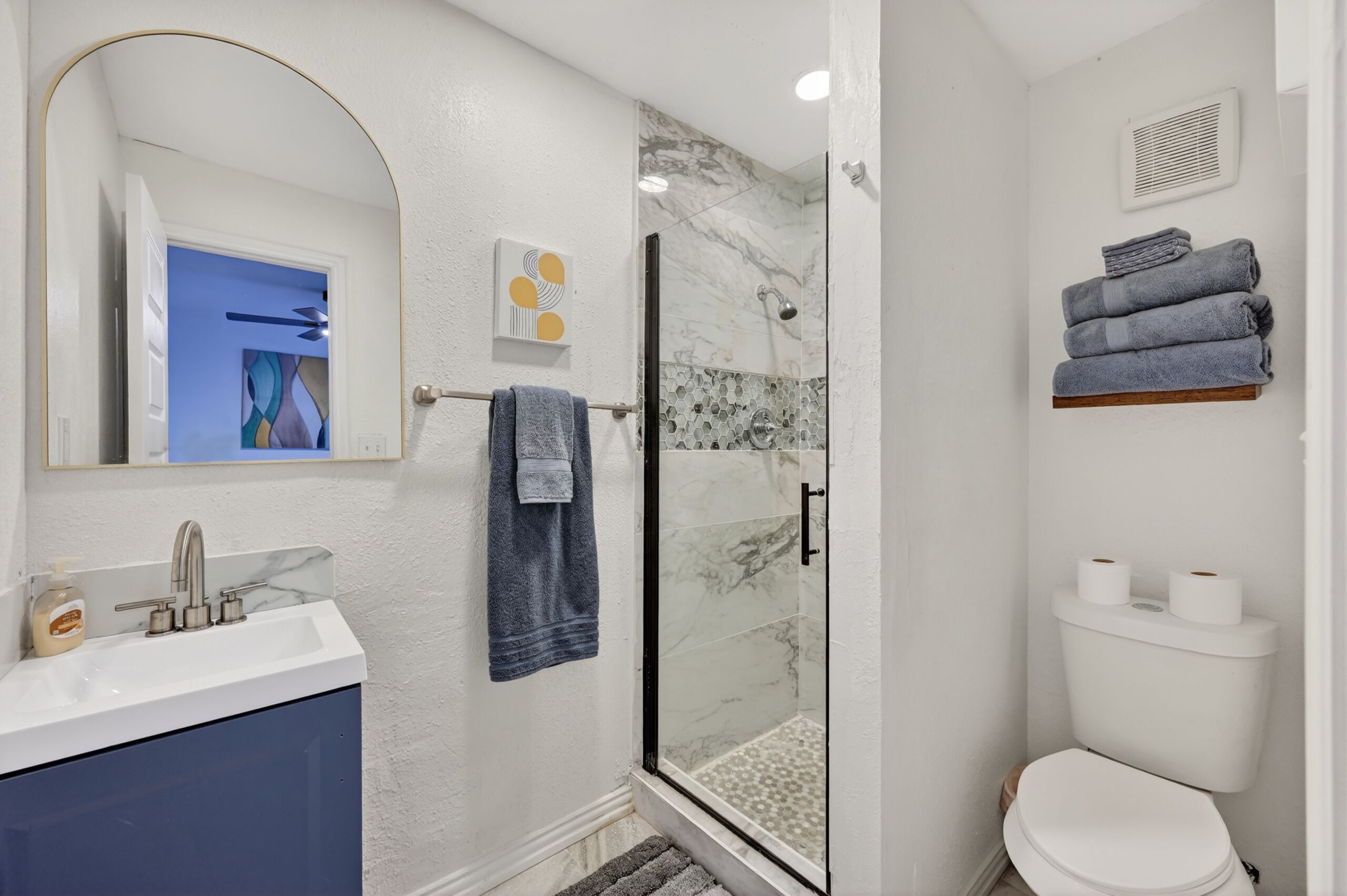 Une salle de bain avec une douche en verre, des toilettes blanches, un lavabo avec un miroir et un porte-serviettes.