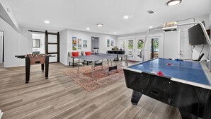 Una habitación amplia con mesa de fútbolín, mesa de ping pong y mesa de billar.