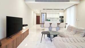 A modern living room with a flat-screen TV, a sofa, a coffee table, and a kitchen in the background. - La Maison 2BR Luxury Apartment Nicosia (Egkomi Lefkosias)