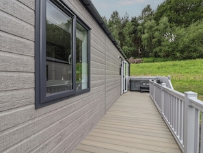 A wooden deck with a white railing, large windows, and a view of a green landscape.
