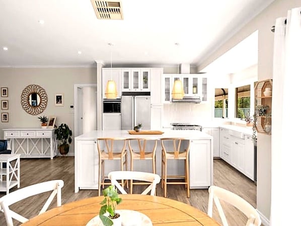 A modern kitchen with white cabinetry, a central island with bar stools, pendant lighting, and a dining area with a wooden table and chairs.