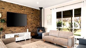 Ein modernes Wohnzimmer mit Backsteinwand, Flachbildfernseher, einer Couch, einem Kamin und einem großen Fenster.