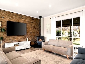 A modern living room with a brick wall, a flat-screen TV, a sofa, a fireplace, and a large window.