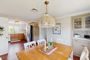 A modern kitchen with wooden cabinets, a dining table with chairs, a chandelier, and a kitchen island. - Mid-Cape Retreat, Near Beaches & Nice Yard (Yarmouth)