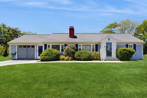 A two-story house with a front garage, a chimney, and a well-maintained lawn. - Mid-Cape Retreat, Near Beaches & Nice Yard (Yarmouth)