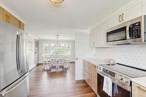 A kitchen with a refrigerator, microwave, stove, and dining table with chairs. - Mid-Cape Retreat, Near Beaches & Nice Yard (Yarmouth)