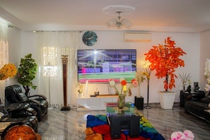 A living room with a flat-screen TV, a sofa, a coffee table, and decorative plants.