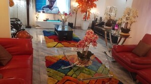 Sala de estar con sofás rojos, una mesa de centro de vidrio, televisor y plantas decorativas.