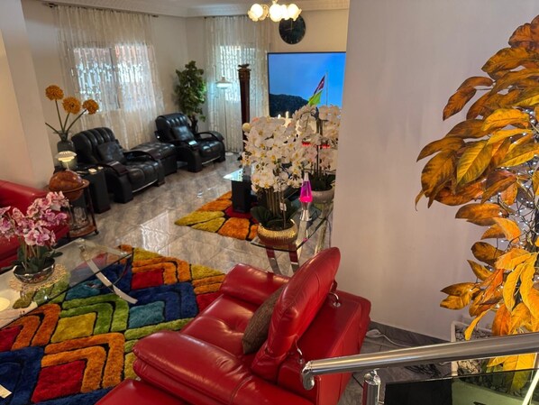 A living room with a red sofa, black leather chairs, a colorful rug, and a large artificial plant.