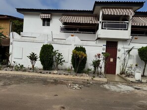 Un edificio de dos pisos con fachada blanca, una puerta marrón y un pequeño balcón con toldo a rayas.