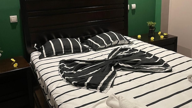 Een bed met gestreepte lakens, een donker hoofdbord en een nachtkastje met een plant.